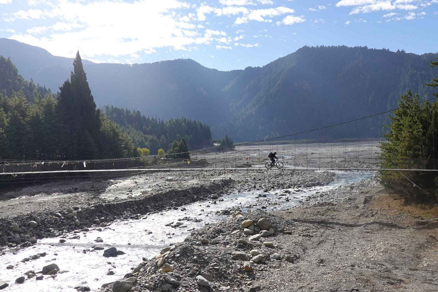 ein mountainbiker fährt im himalaya über eine hängebrücke