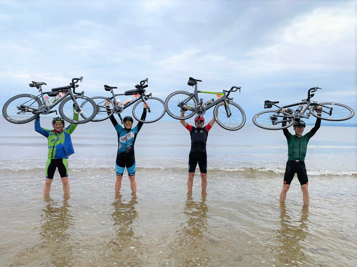 Vier Rennradfahrer stehen mit ihren Rädern in der Ostsee